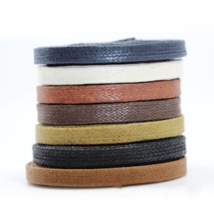May include: A stack of eight different coloured leather cords. The cords are all the same width and are arranged in a circle. The colours are navy blue, white, red, brown, olive green, black, and brown.