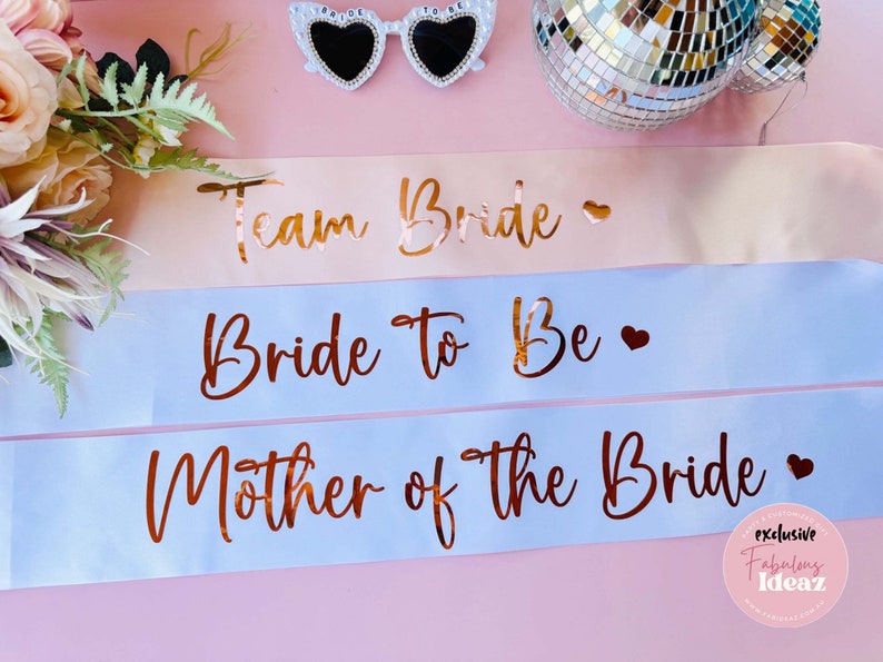 Peut inclure: Trois sashes en satin avec inscription en or. La premi&egrave;re est rose et dit "Team Bride". La deuxi&egrave;me est bleu clair et dit "Bride to Be". La troisi&egrave;me est bleu clair et dit "Mother of the Bride".