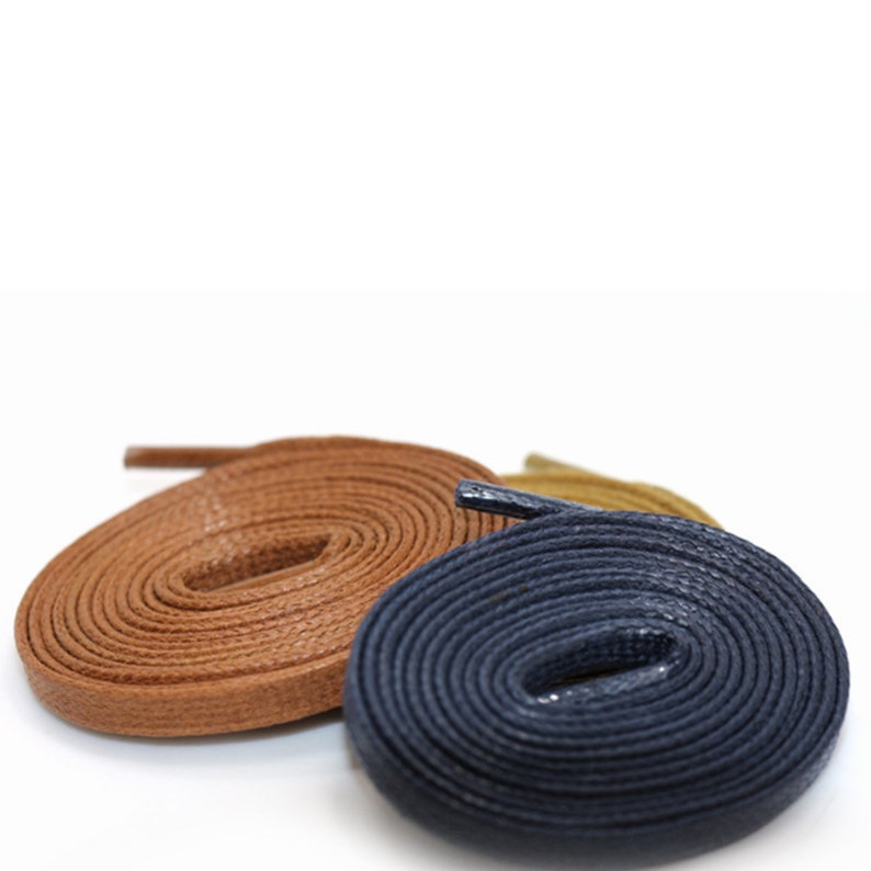 May include: Three spools of shoelaces in different colours: brown, blue, and tan. The shoelaces are made of a textured material and are coiled up.