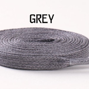 May include: A close-up of a grey shoelace, coiled and ready to be used. The shoelace is made of a woven material and has a slightly textured surface.