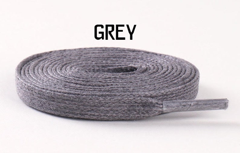 May include: A close-up of a grey shoelace, coiled and ready to be used. The shoelace is made of a woven material and has a slightly textured surface.