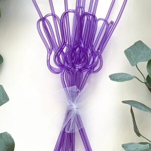 May include: A bunch of purple plastic drinking straws tied together with a white ribbon. The straws are bent into a heart shape.
