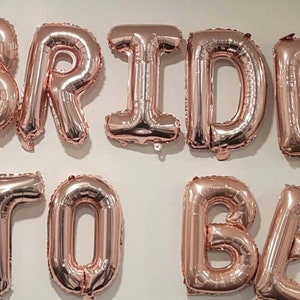 May include: Rose gold foil letter balloons spelling "BRIDE TO BE".