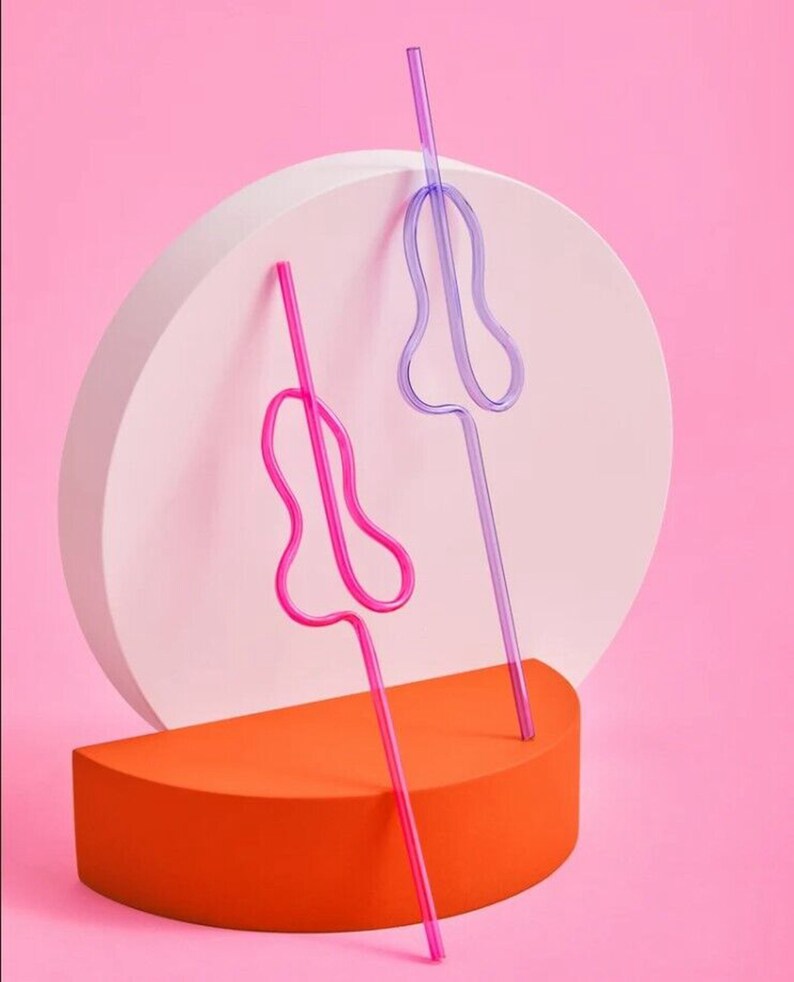 May include: Two colorful, flexible drinking straws with a unique, curved design. The straws are pink and purple and are standing upright on a white and orange platform.