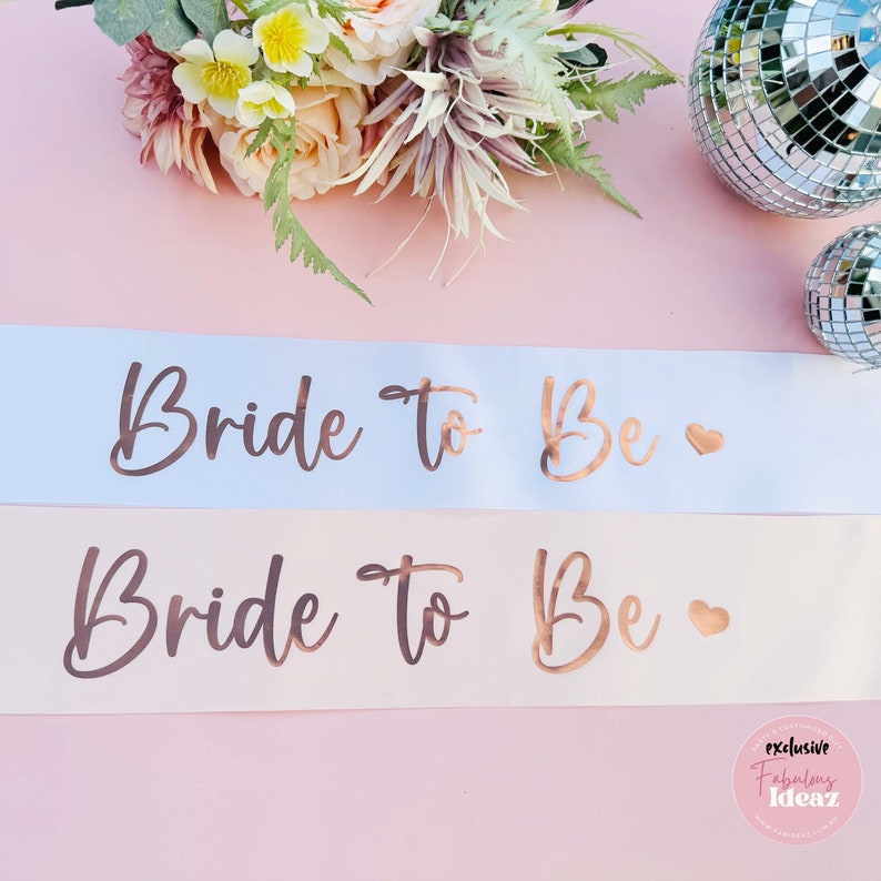 Two bride to be sashes on a pink background.