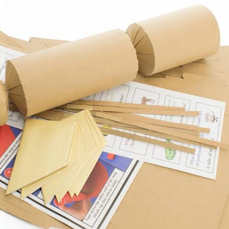 May include: A disassembled brown paper Christmas cracker kit. The kit includes the cracker's cylindrical body, paper strips, and printed game cards. The text on the game cards is partially visible.