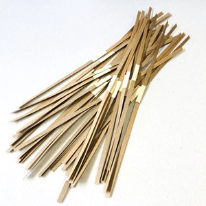May include: A collection of thin, brown paper strips, each with a small section of tan tape. The strips are arranged in a loose, overlapping pattern against a white background. The paper appears to be a natural, unbleached color.