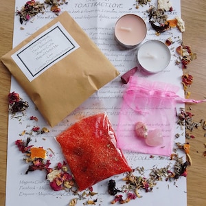May include: A spell kit for love containing a brown paper packet labelled Magenta Crafts, a clear plastic bag of red granular material, two tea light candles, a purple incense cone, and two pink crystals inside a small pink organza drawstring bag.