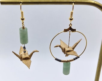 May include: A pair of gold origami crane earrings with green jade stone accents. One earring features a hoop with a crane suspended inside, while the other has a crane dangling from a jade stone.