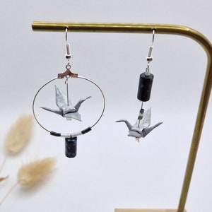 May include: A pair of silver earrings with black and white beads and a silver origami crane hanging from each earring.