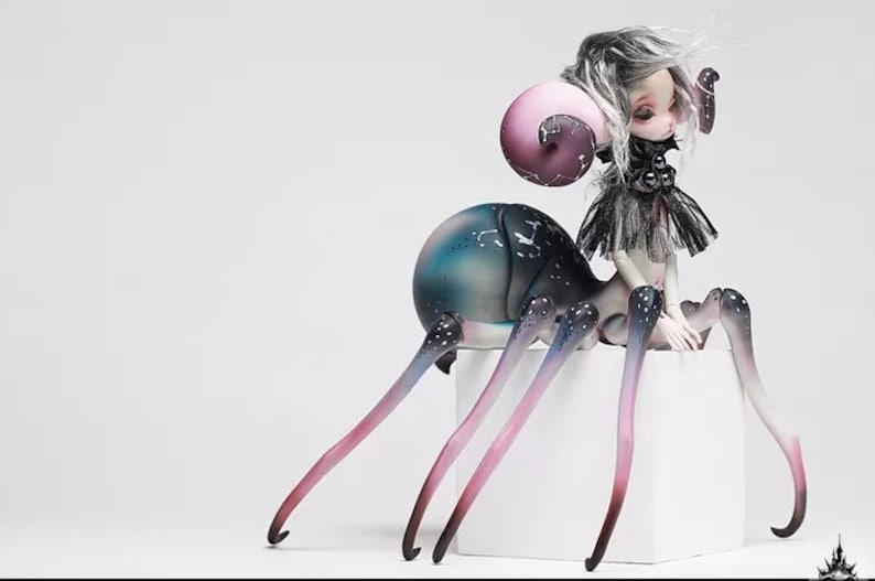 May include: A unique art doll with a spider-like body and a human-like upper body. The doll features a large, bulbous abdomen with blue and green hues, long legs with pink and purple gradients, and a small black dress.
