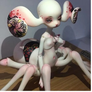 May include: A unique art doll with a pale complexion, large eyes, and a spider-like body. The doll has long, curved appendages and is adorned with intricate painted details, including floral and bird motifs.