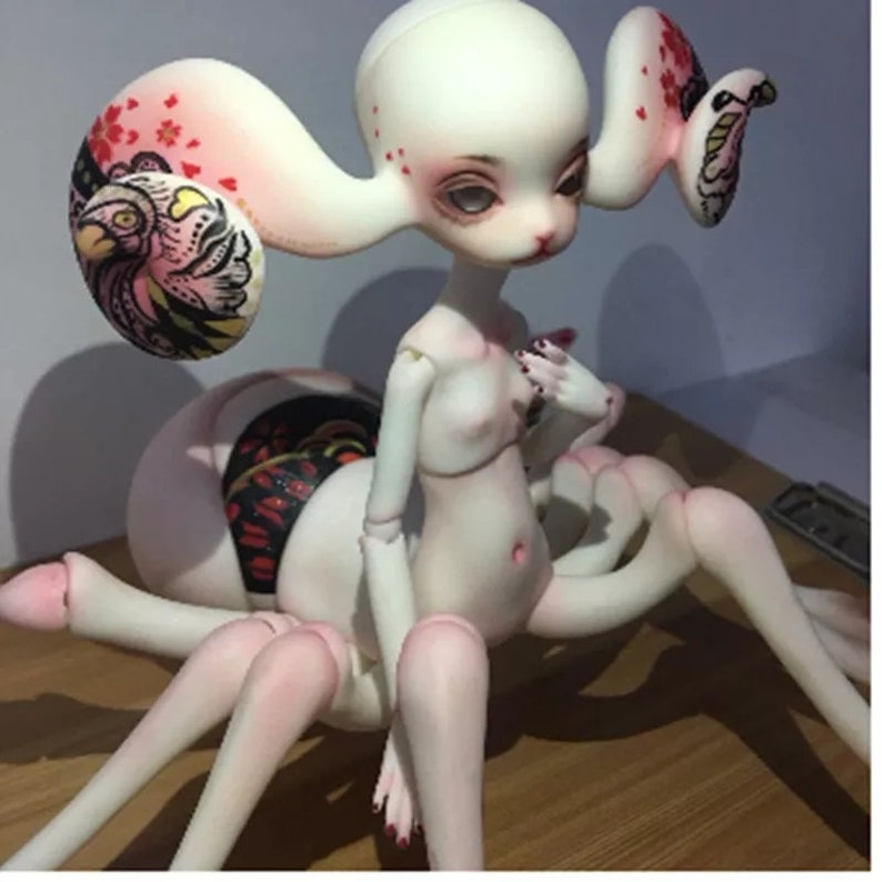 May include: A unique art doll with a pale complexion, large eyes, and a spider-like body. The doll has long, curved appendages and is adorned with intricate painted details, including floral and bird motifs.