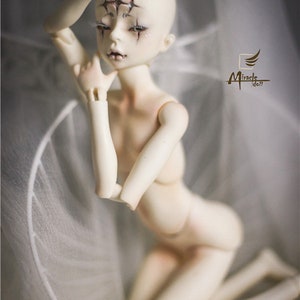 May include: A pale-skinned ball-jointed doll with detailed facial features, including dark eye makeup and star-shaped markings on the forehead. The doll is posed kneeling, with one arm raised. The Miracle Doll logo is visible.