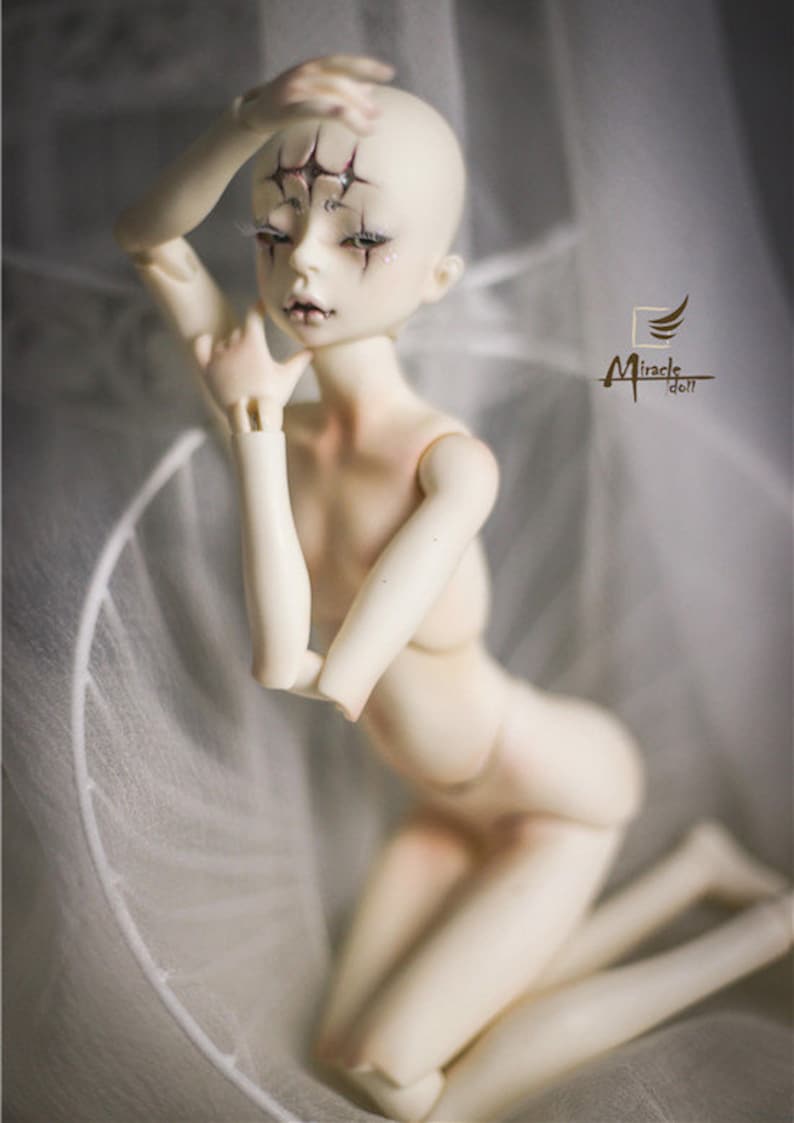 May include: A pale-skinned ball-jointed doll with detailed facial features, including dark eye makeup and star-shaped markings on the forehead. The doll is posed kneeling, with one arm raised. The Miracle Doll logo is visible.
