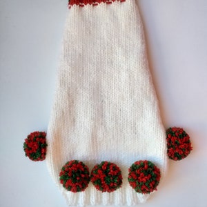 Puede incluir: Un su&eacute;ter blanco tejido para perros con un cuello a rayas rojas y verdes y pompones rojos y verdes. El su&eacute;ter tiene un dobladillo acanalado y est&aacute; dise&ntilde;ado para adaptarse a un perro peque&ntilde;o. Los pompones est&aacute;n espaciados uniformemente a lo largo del borde inferior.