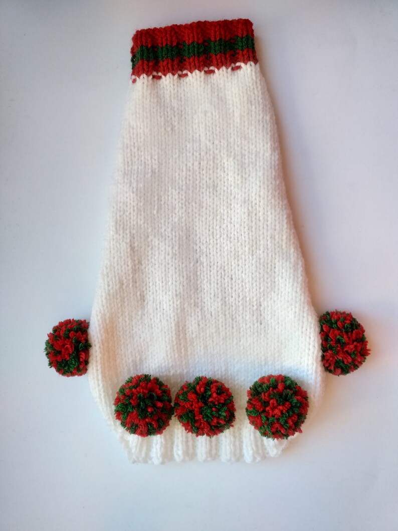 Puede incluir: Un su&eacute;ter blanco tejido para perros con un cuello a rayas rojas y verdes y pompones rojos y verdes. El su&eacute;ter tiene un dobladillo acanalado y est&aacute; dise&ntilde;ado para adaptarse a un perro peque&ntilde;o. Los pompones est&aacute;n espaciados uniformemente a lo largo del borde inferior.