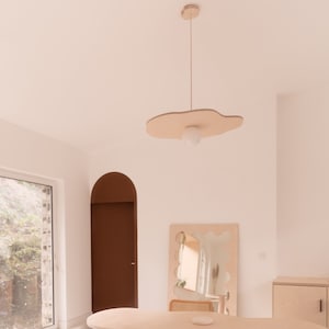 Puede incluir: Una mesa de madera clara con una forma org&aacute;nica y una silla de cuero marr&oacute;n. La mesa tiene una superficie blanca y est&aacute; sostenida por cuatro patas de madera. La silla tiene un marco de cromo y est&aacute; colocada a la derecha de la mesa. Un peque&ntilde;o taburete de madera est&aacute; en primer plano. La habitaci&oacute;n tiene paredes blancas y una gran ventana con vista a los &aacute;rboles.