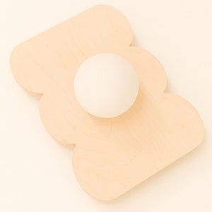 May include: A white ball sits on a light brown wooden tray shaped like a cloud.