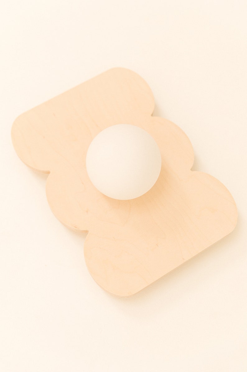 May include: A white ball sits on a light brown wooden tray shaped like a cloud.