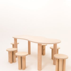 May include: A set of six wooden stools and a large, organic-shaped wooden table. The table and stools are all made of light-colored wood and have a natural finish.
