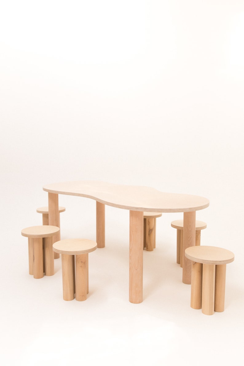 May include: A set of six wooden stools and a large, organic-shaped wooden table. The table and stools are all made of light-colored wood and have a natural finish.