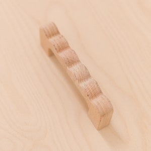 Puede incluir: Un pomo de madera para armario con un borde decorativo festoneado. El pomo es de color marr&oacute;n claro y tiene un dise&ntilde;o simple y elegante.