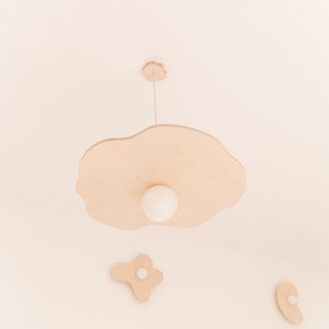 Puede incluir: Una l&aacute;mpara de madera con forma de nube con una bombilla blanca que cuelga del techo. Hay tres nubes de madera m&aacute;s peque&ntilde;as en el techo.