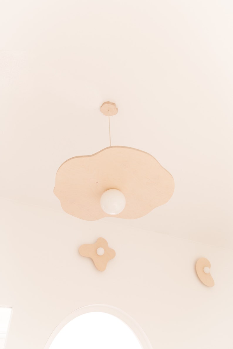 Puede incluir: Una l&aacute;mpara de madera con forma de nube con una bombilla blanca que cuelga del techo. Hay tres nubes de madera m&aacute;s peque&ntilde;as en el techo.