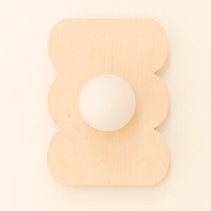 May include: A white egg sits in the center of a wooden egg holder shaped like a flower. The holder is light brown and has a scalloped edge.