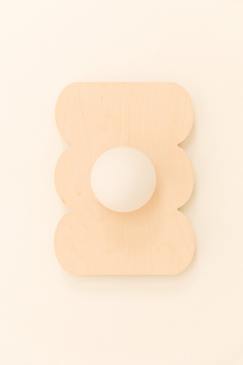 May include: A white egg sits in the center of a wooden egg holder shaped like a flower. The holder is light brown and has a scalloped edge.