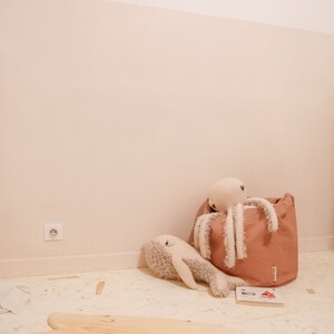 May include: A wooden surfboard-shaped balance board with a light brown finish. The board is on a light beige floor with a stuffed octopus and whale toy in the background.