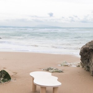 May include: White organic shaped coffee table with four wooden legs on a sandy beach.
