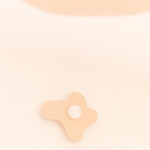 Pu&ograve; includere: Un decoro da parete in legno di colore marrone chiaro, di forma irregolare e astratta, con un cerchio bianco al centro.