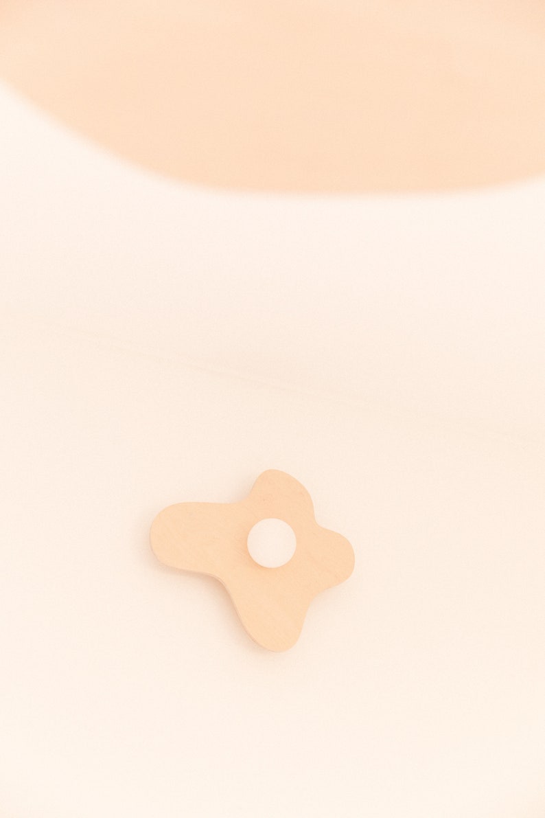 Pu&ograve; includere: Un decoro da parete in legno di colore marrone chiaro, di forma irregolare e astratta, con un cerchio bianco al centro.