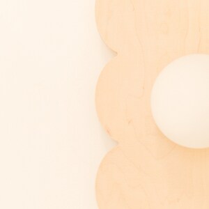 May include: A light brown wooden cutout of a flower with a round hole in the center.