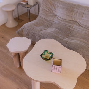May include: Two wooden tables with unique, organic shapes. The larger table has a green glass bowl and a pink and black box on top. The smaller table is round with three legs.