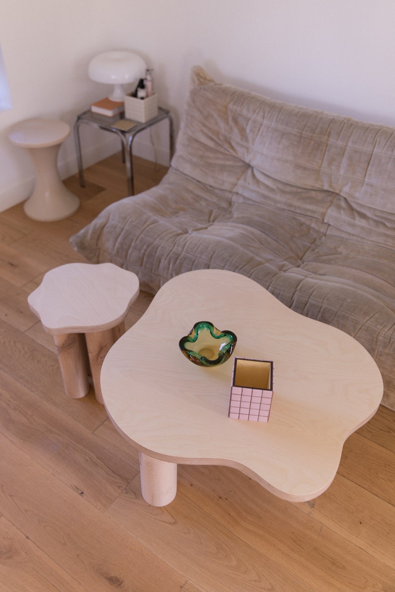 May include: Two wooden tables with unique, organic shapes. The larger table has a green glass bowl and a pink and black box on top. The smaller table is round with three legs.