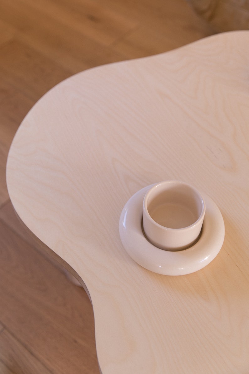 May include: A white ceramic cup and saucer set on a light wood table.