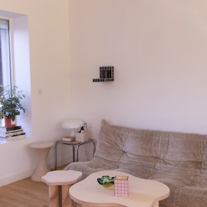 May include: Two wooden coffee tables with irregular cloud-like tops. The larger table has a pink and yellow patterned box and a green glass bowl on top. The smaller table is next to the larger table. Both tables have thick wooden legs.