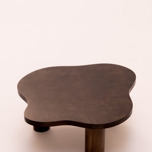 May include: A dark brown wooden coffee table with an irregular, cloud-like shape and three legs.