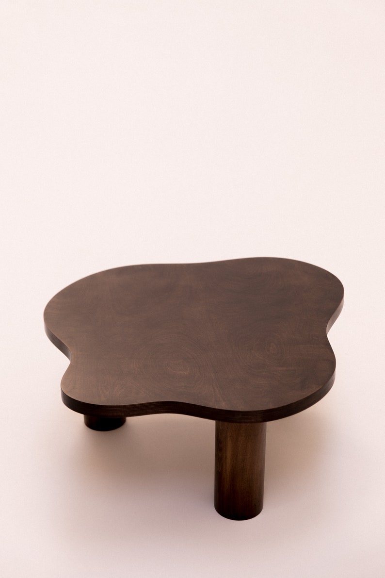 May include: A dark brown wooden coffee table with an irregular, cloud-like shape and three legs.