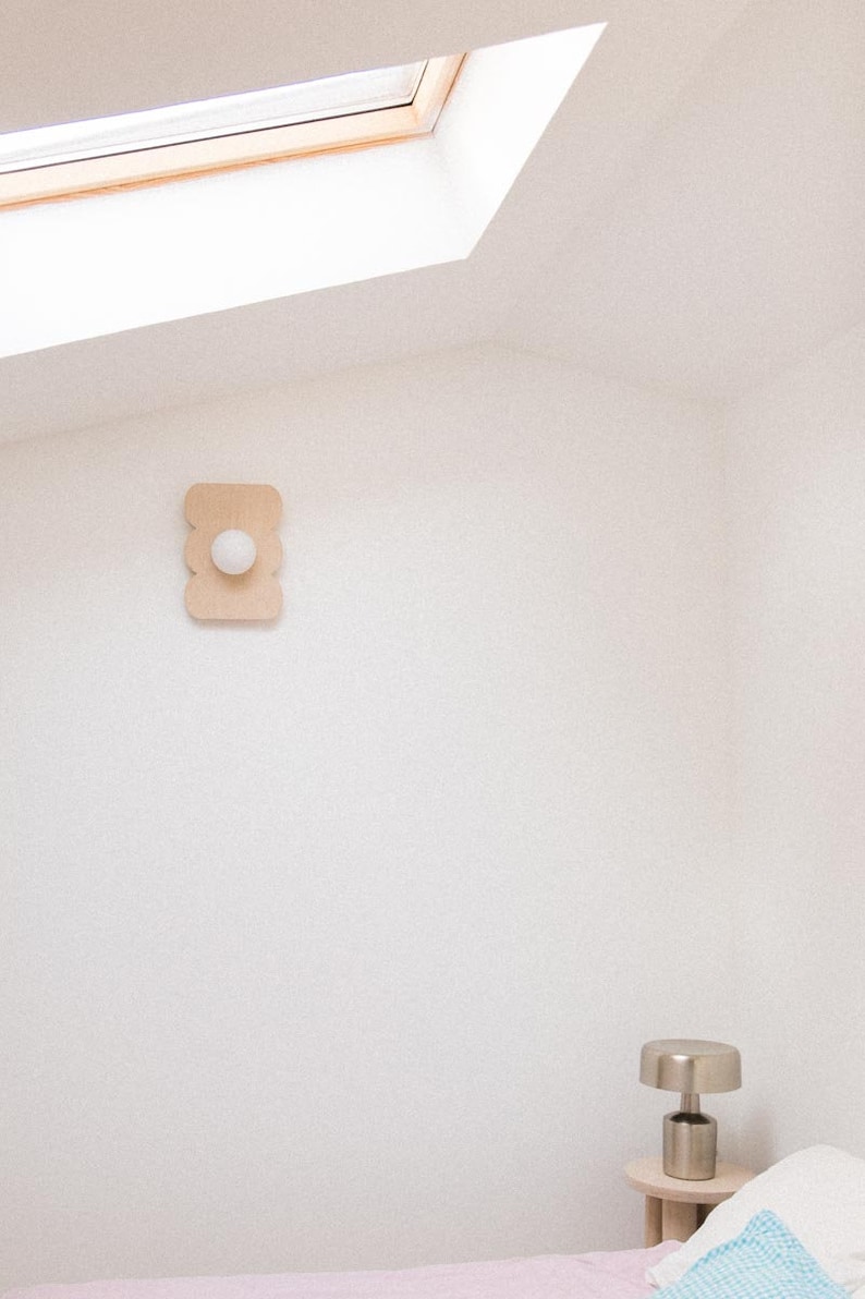 May include: A white ceiling with a skylight and a white wall with a wooden wall sconce with a white light bulb. A small table with a silver lamp sits in the corner of the room.