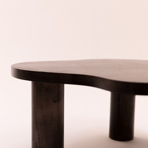 May include: A dark brown wooden coffee table with an organic, free-form shape and three cylindrical legs.