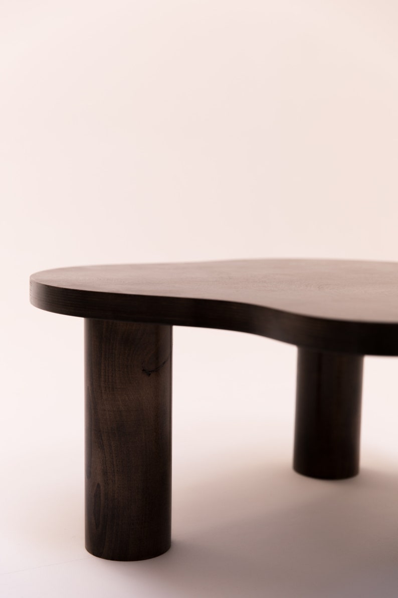 May include: A dark brown wooden coffee table with an organic, free-form shape and three cylindrical legs.