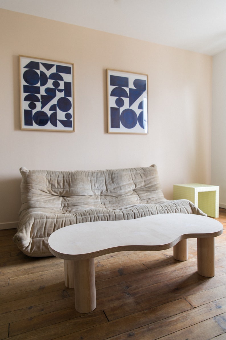 May include: A light beige sofa with a white, organic-shaped coffee table with three legs. The coffee table is in front of the sofa and there is a small, light green side table to the right of the sofa.