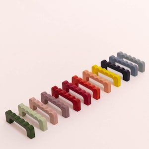 Peut inclure: Un ensemble de 14 boutons de cabinet colorés avec un design à bord festonné. Les boutons sont disposés en rangée du vert au bleu.