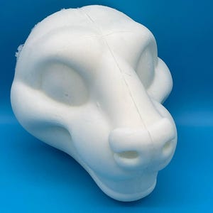 Könnte beinhalten: Ein weißer Schaumstoff-Rohling für einen Pelz-Kopf mit einem definierten Maul, Nase und Augen. Der Kopf ist für die Herstellung von Pelzkostümen gedacht.