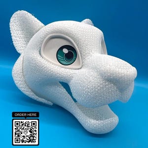 May include: A white, textured lion head sculpture with large, teal-colored eyes. The sculpture has an open mouth and is set against a blue background. A small black square with the text "ORDER HERE" and a QR code is in the lower left corner.
