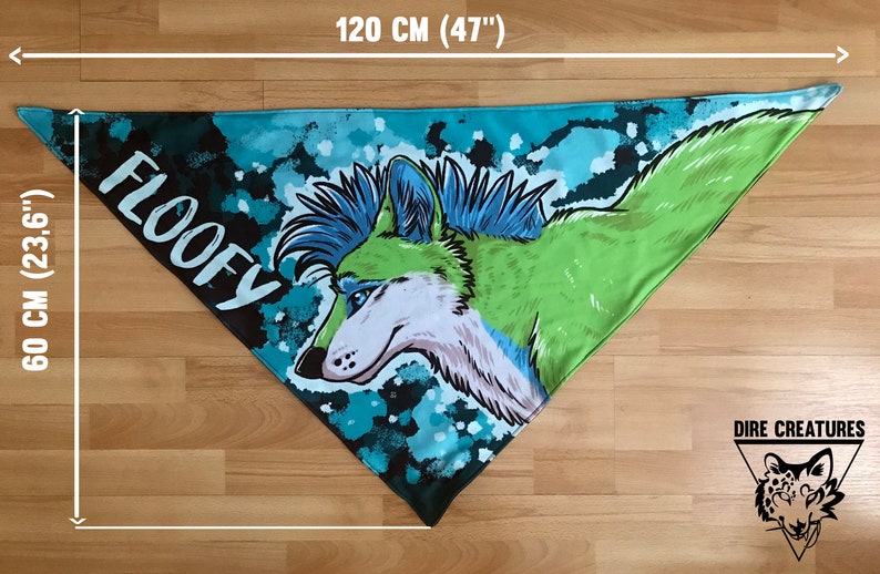 May include: A triangular bandana with a green and blue wolf illustration and the word "FLOOFY" printed on it. The bandana measures 60 cm by 120 cm. The bandana is on a wooden surface.